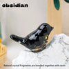 A glossy black obsidian bird statue resting on a white marble surface.