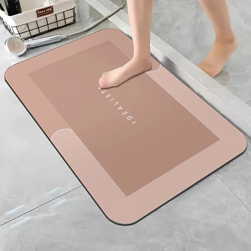 A beige diatomaceous earth absorbent bath mat is placed on a gray floor next to a person's bare foot.