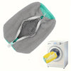 A gray mesh shoe wash bag with a zipper is shown next to a white washing machine.