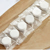 A row of white disposable compressed travel towels packaged in clear plastic on a wooden surface.