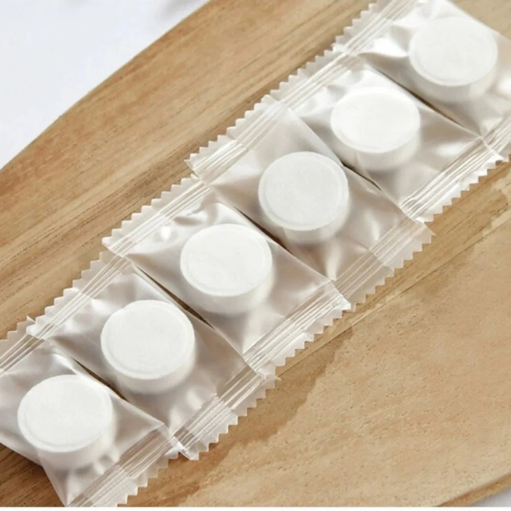 A row of white disposable compressed travel towels packaged in clear plastic on a wooden surface.