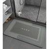 A rectangular gray anti-slip floor mat is placed on a dark tile floor in a modern bathroom setting.