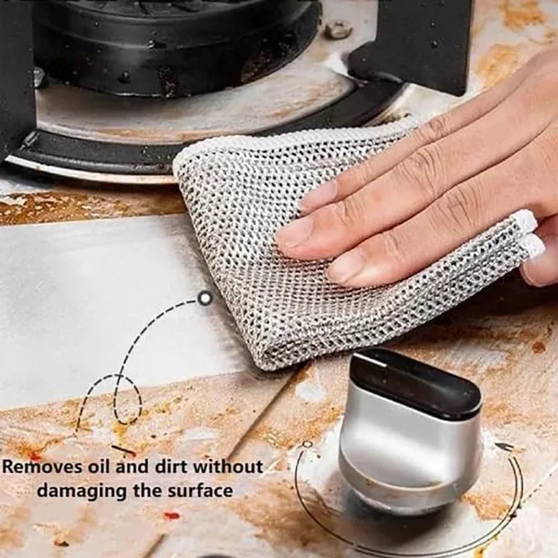 A hand is using a thick metal wire cleaning cloth to remove oil and dirt from a surface.