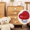 Un bouton de chasse d'eau en forme de cœur rouge à côté d'une commode en bois et d'un ours en peluche blanc.