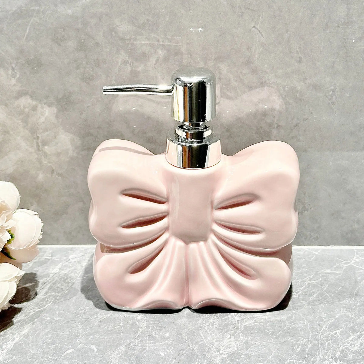 A pink ceramic pump dispenser bottle with a bowknot design sits on a gray surface.
