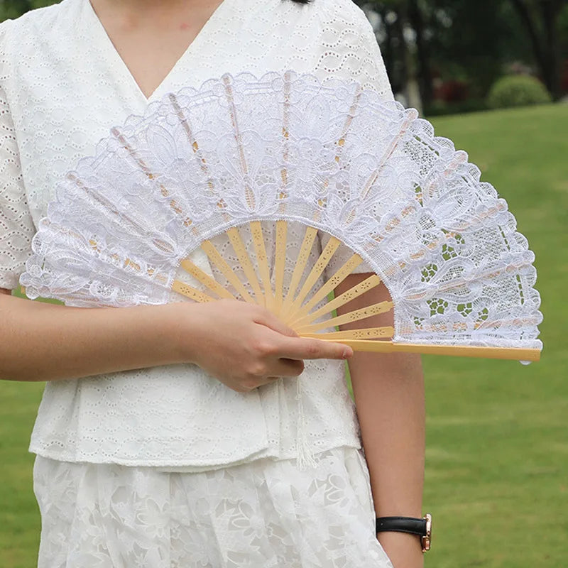 A woman holds an elegant white lace folding hand fan with gold accents outdoors.
