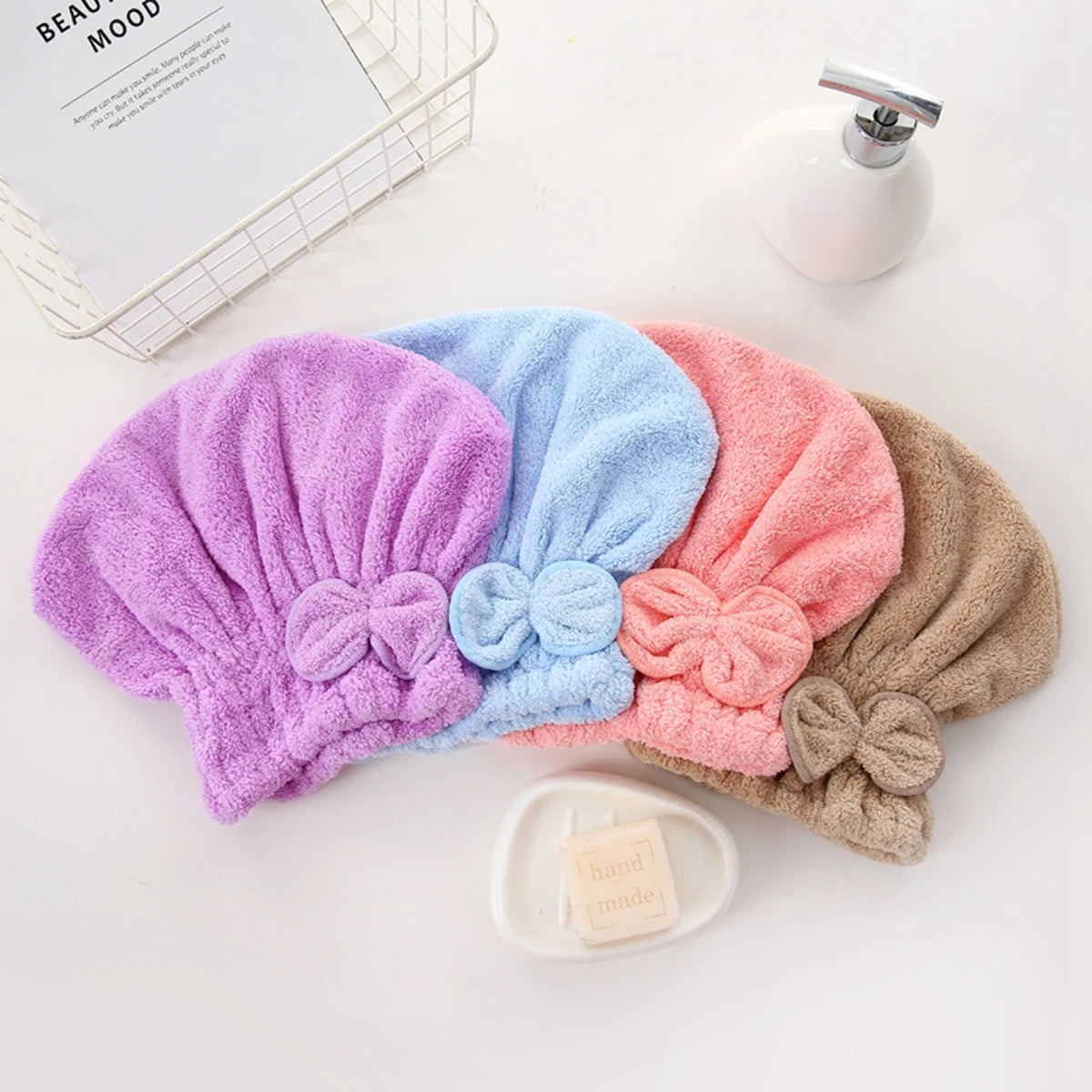 A collection of purple, blue, pink, and beige microfiber hair drying caps and towels displayed on a white surface.