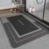 A rectangular gray anti-slip floor mat with the word HOME printed on it, placed on a light tiled floor.