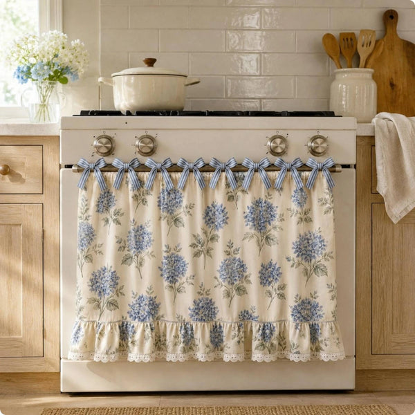 A white farmhouse floral oven door skirt with blue and green foliage and tied fabric accents.