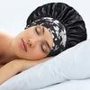 Una mujer duerme con un gorro de satén negro en la cabeza, apoyada en una almohada blanca.