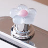 A flower-shaped toilet flush button with translucent white and pink elements resting on a chrome surface.