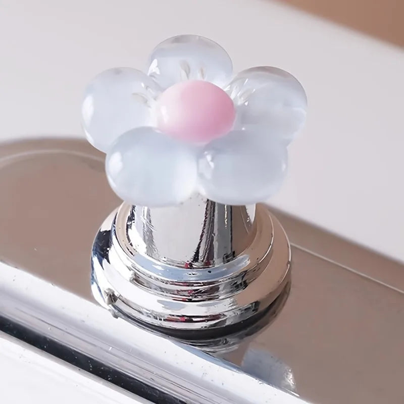 A flower-shaped toilet flush button with translucent white and pink elements resting on a chrome surface.