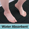 A close-up of a foot resting on a black absorbent bath mat, showing water absorption.