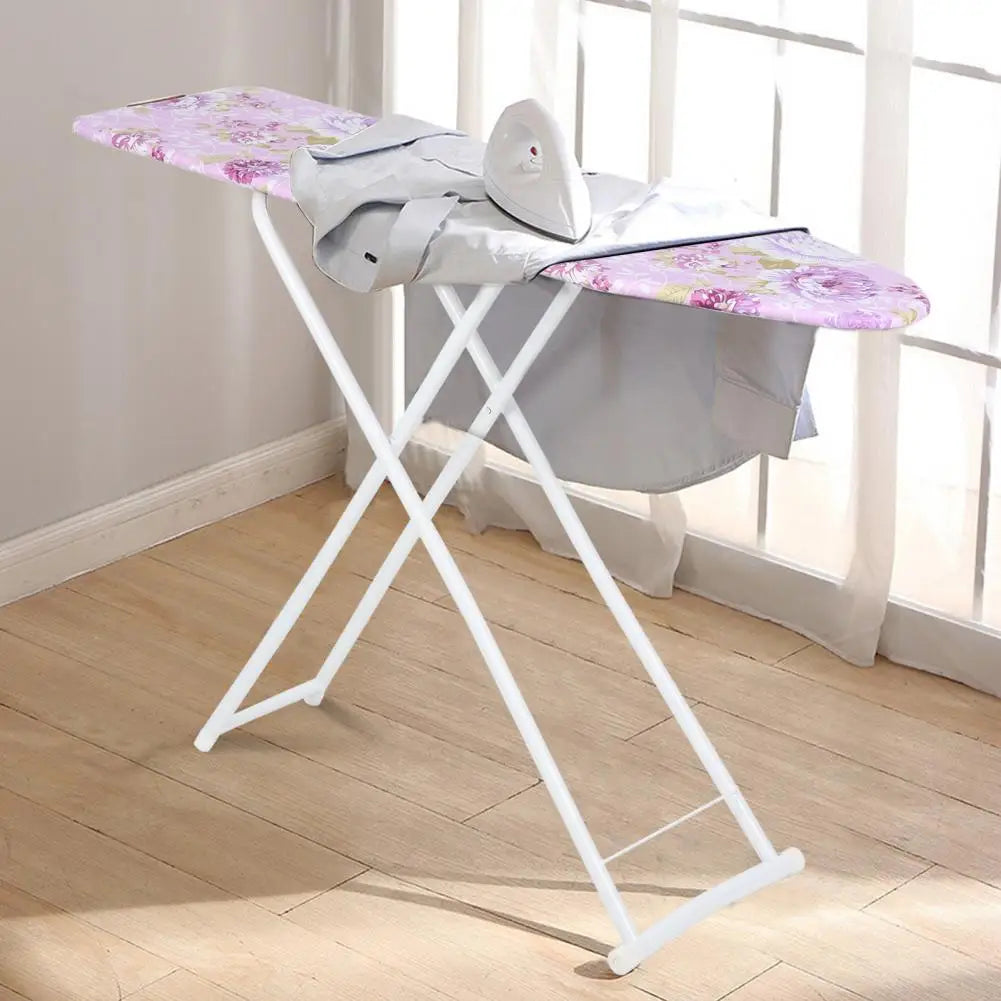Una tabla de planchar blanca plegable con funda floral morada junto a una ventana.