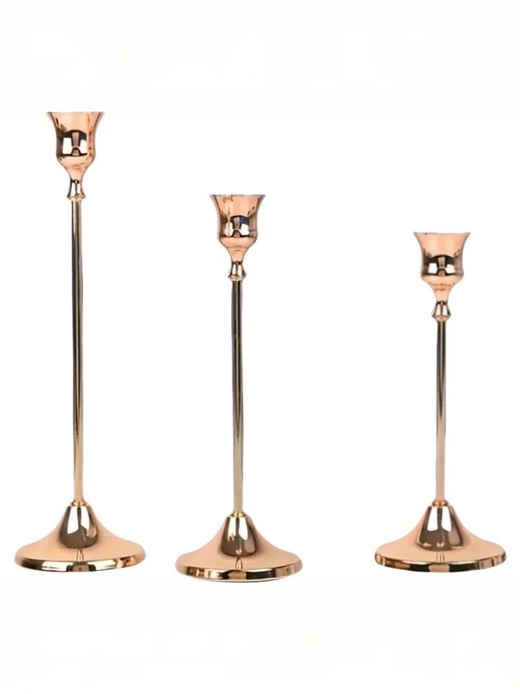 A set of three elegant rose gold metal candle holders with slender stems and flared bases.