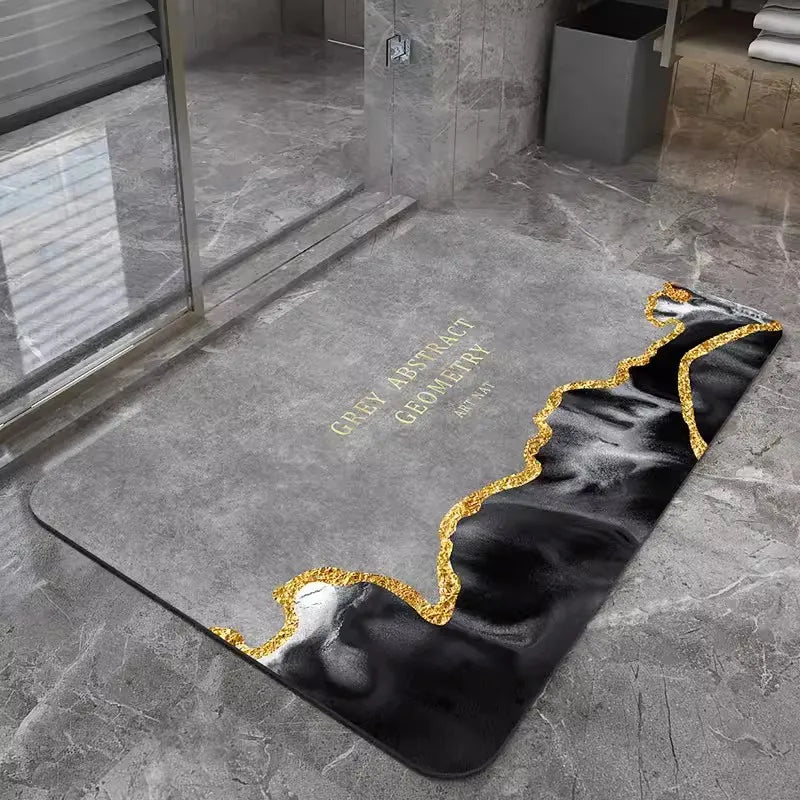 A black and white abstract geometric bath mat with gold trim placed on a gray stone floor.