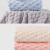 A stack of four thickened microfiber bath towels in pastel colors: pink, cream, light blue, and gray.