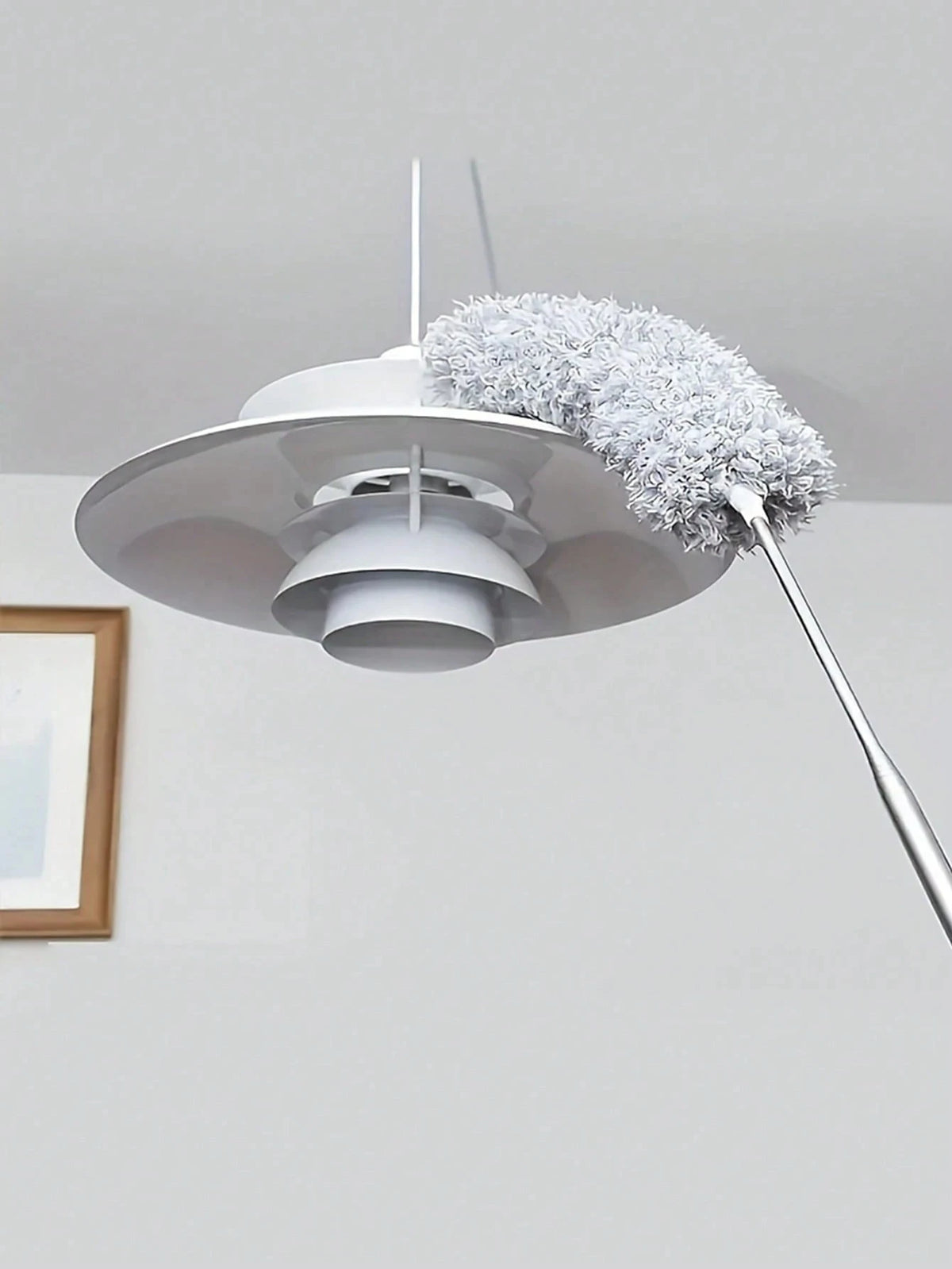 A white flexible microfiber cleaning duster brush with a fluffy gray head is suspended from the ceiling.