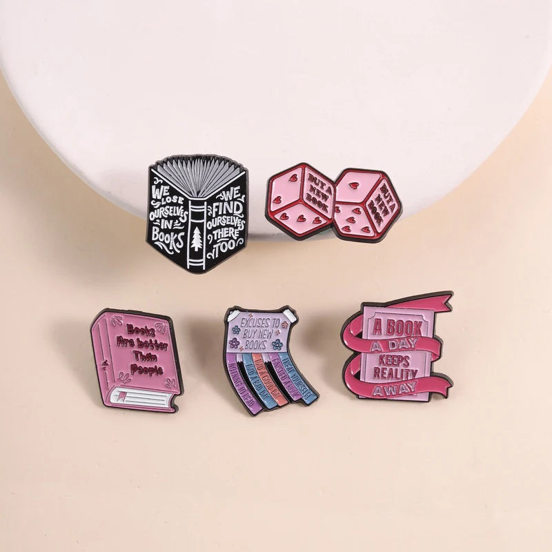 Colección de pines de esmalte con texto sobre lectura y libros, incluyendo un pin negro con diseño de árbol y pi rosa