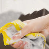 A hand is squeezing a yellow reusable double-sided dishwashing sponge set covered in white soap bubbles.