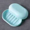 A light blue portable soap holder with a lid is shown resting on a gray surface.