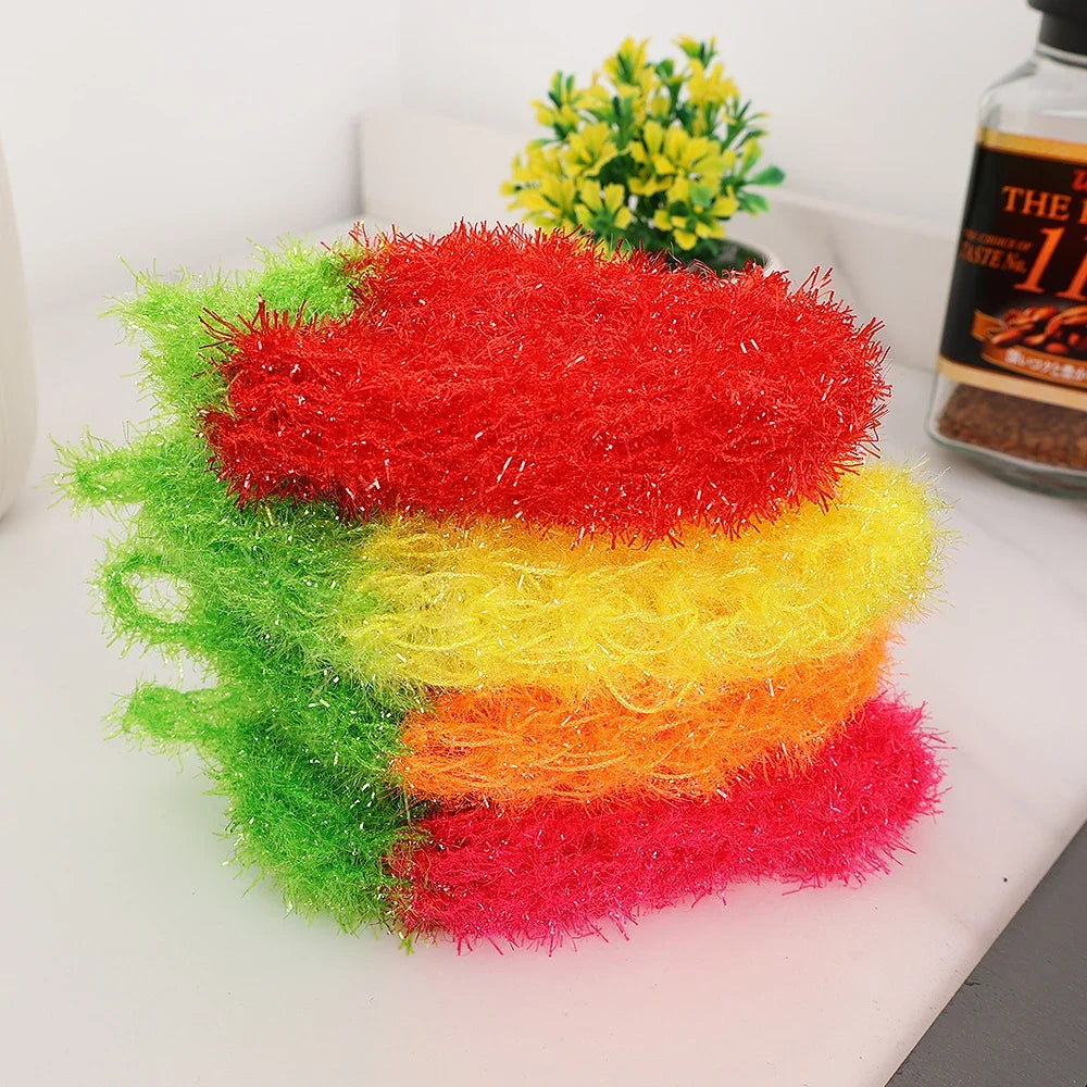 A stack of brightly colored strawberry scrubber sponges in red, yellow, and green are displayed next to a bottle.
