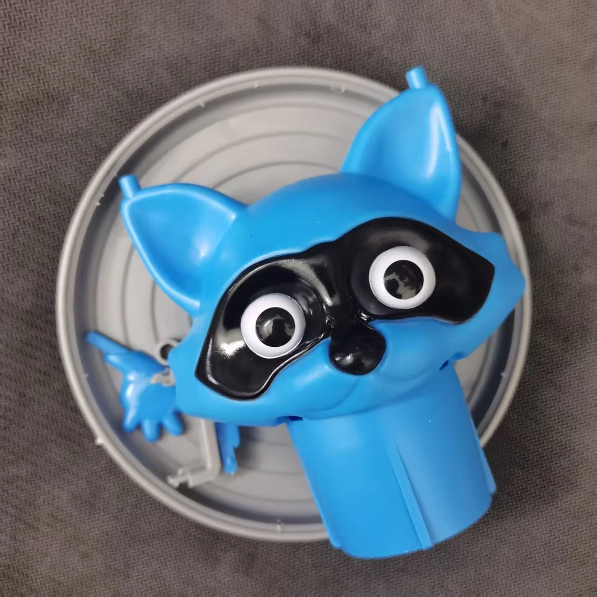 A blue decorative toilet paper holder shaped like a cat's face with large white eyes and black markings, resting on a silver 