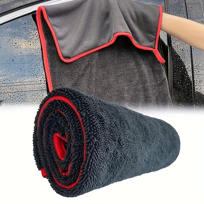 A rolled black microfiber car drying towel with red trim is shown next to a hand holding a car door.