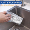 A hand is holding a white, porous cleaning pad in a stainless steel kitchen sink.