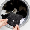 Hands are removing pet hair from a black felted cat-shaped sponge inside a circular container.
