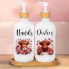 Two white soap dispensers with wooden caps and pump tops featuring a decorative brown cow print design.