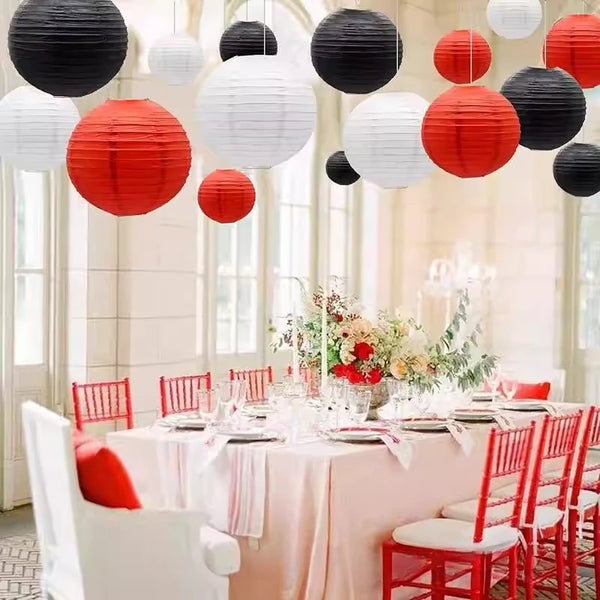 A table decorated with pink linen and white floral arrangements surrounded by red chairs and overhead paper lanterns.