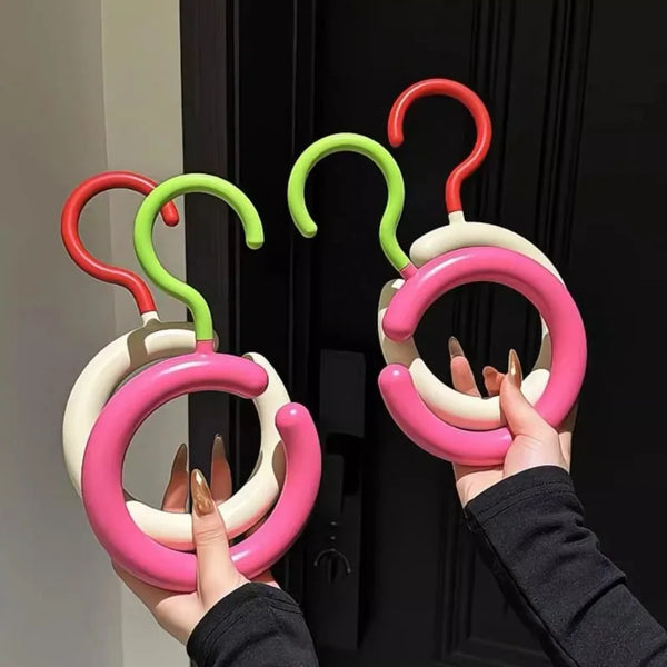 A hand is holding a colorful invisible multi-function coat and hat hanger with red, green, and pink rings.