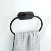 Estante adhesivo de toallas de acero inoxidable negro montado en pared blanca, sosteniendo una toalla gris texturizada.