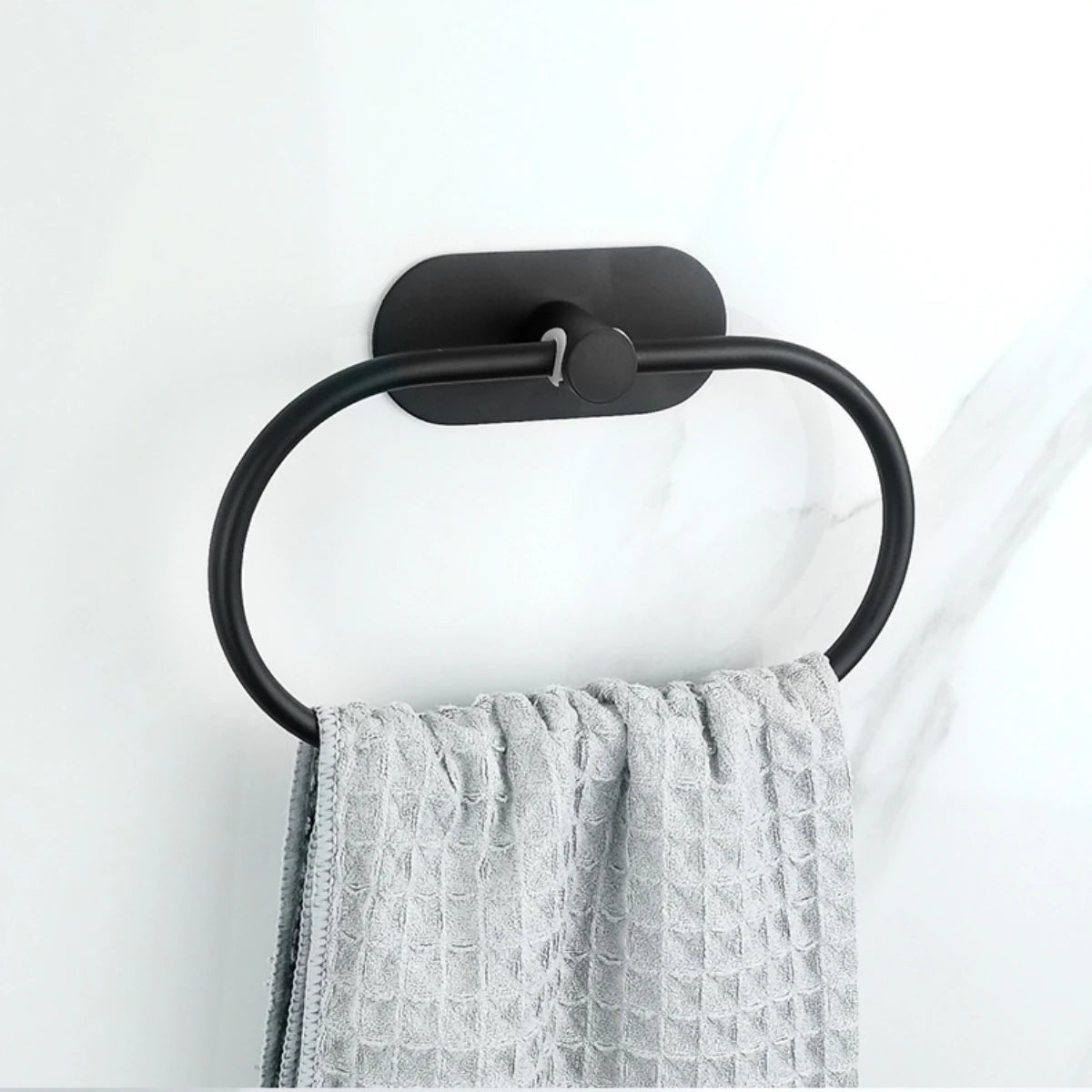 Estante adhesivo de toallas de acero inoxidable negro montado en pared blanca, sosteniendo una toalla gris texturizada.