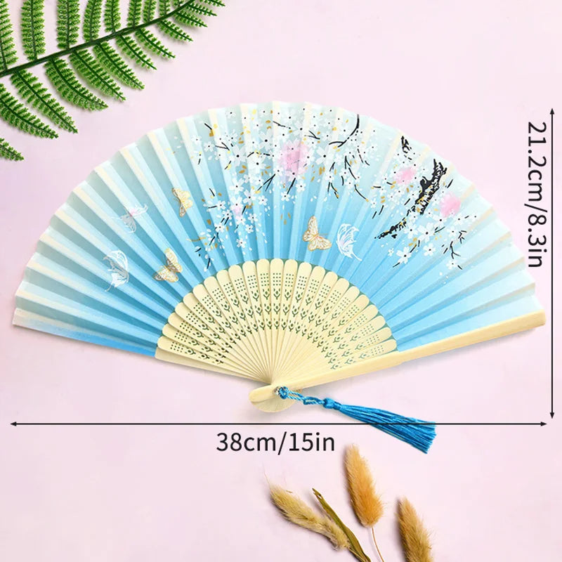 Light blue lace fabric folding hand fan with floral accents shown against a pink background.