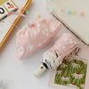 A pink embroidered sun umbrella resting on a white surface next to a notebook and a white grid.