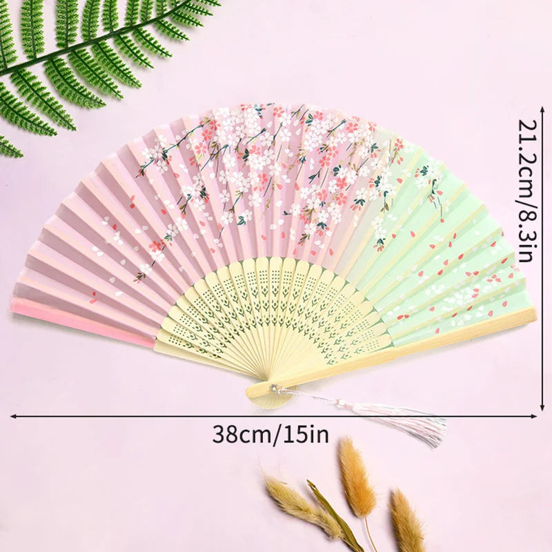 Pink and green lace fabric folding hand fan with floral patterns displayed on a light purple background.