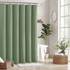 A set of light sage green waffle weave shower curtains hanging on a metal rod in a bathroom setting.