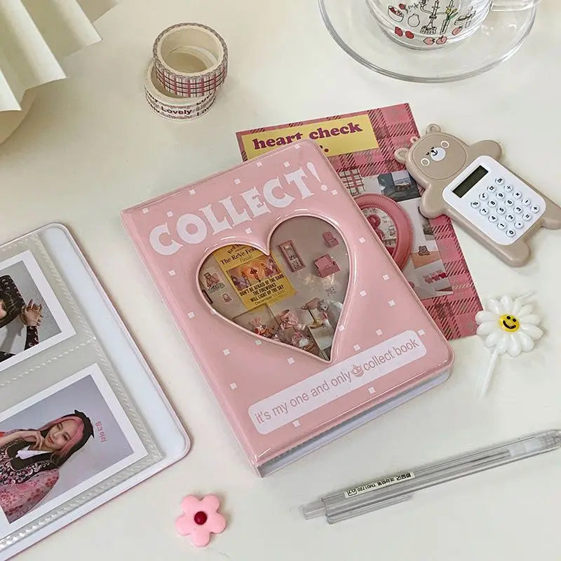 Álbum de fotos en forma de corazón rosa titulado 'Collect' con varios objetos pequeños y un lápiz de color claro cercano.