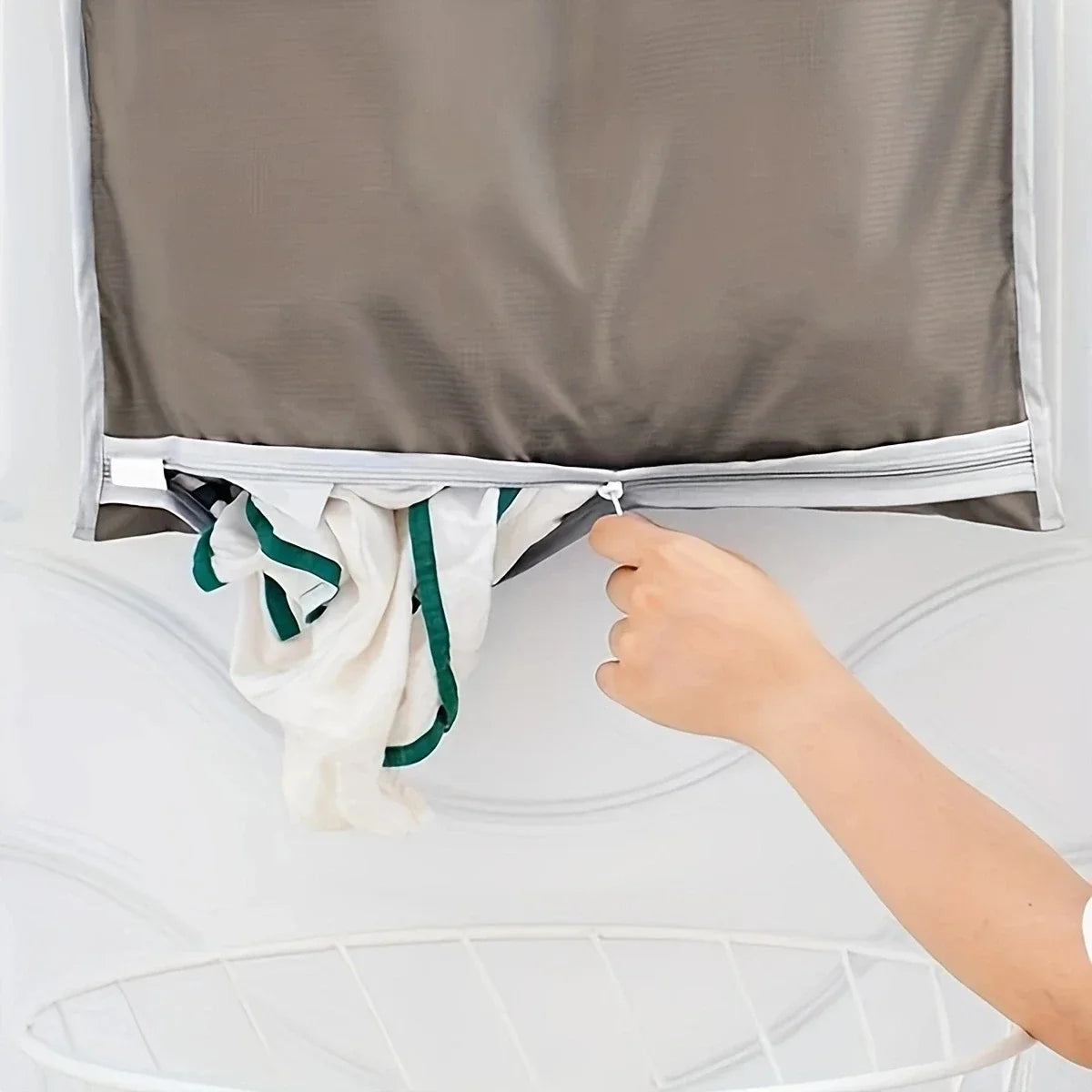 A hand is opening a gray fabric laundry organizer to hang white towels.