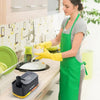 Une femme portant un tablier vert utilise un distributeur de liquide vaisselle jaune sur un comptoir en bois.