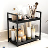 A black two-tier desktop storage rack holding various glass and ceramic beauty products like bottles and brushes.