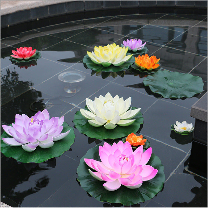 A collection of artificial lotus flowers in various colors including pink, yellow, and orange floating on dark water.