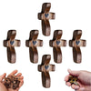 Colección de cruces de bolsillo de madera en varios tamaños y acabados, junto a una mano sosteniendo una cruz pequeña.