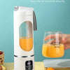 Una licuadora batidora eléctrica portátil blanca para zumos de fruta, junto a fruta fresca y un vaso de jugo de naranja.