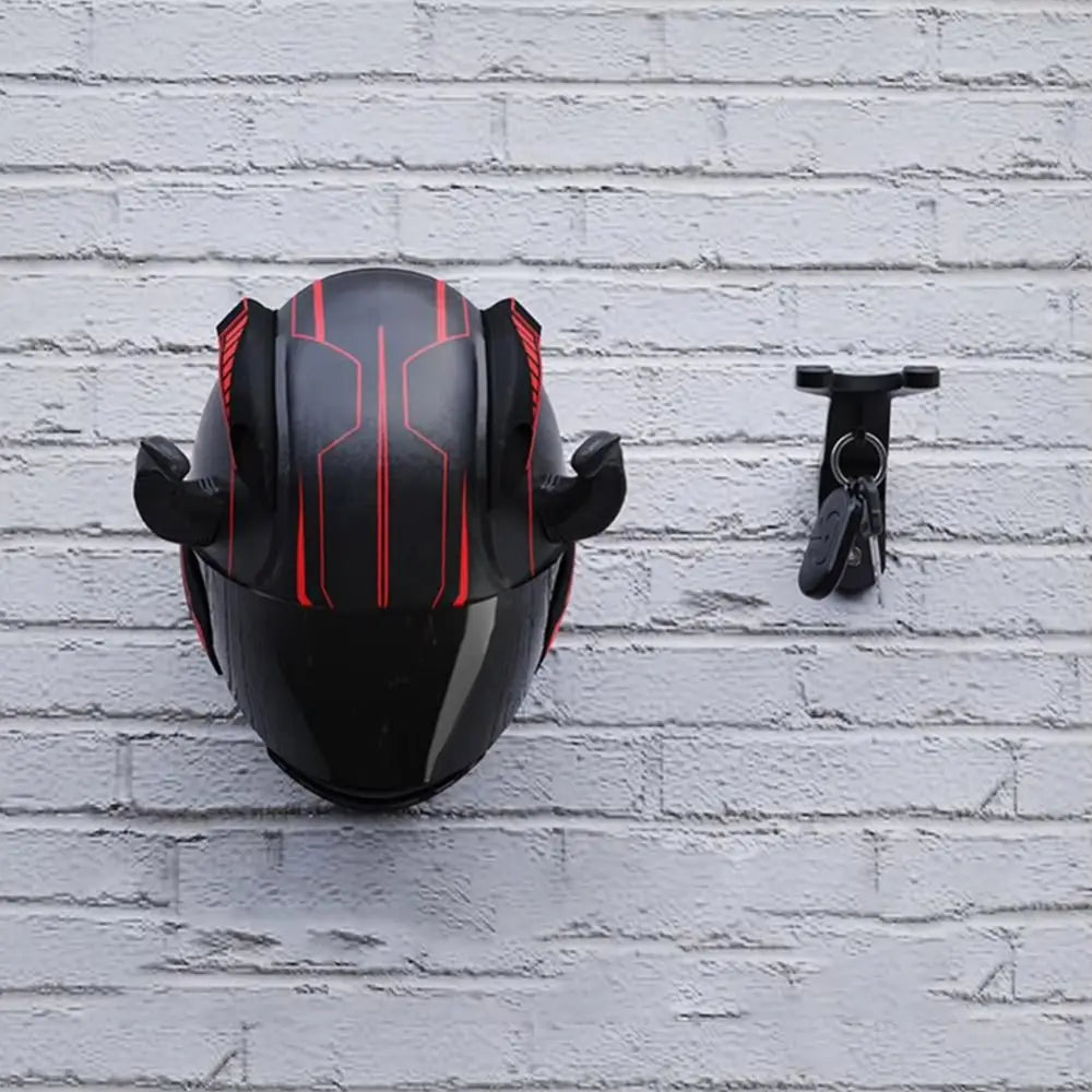 A black wall hook with red accents is mounted on a white brick wall, next to a small black hook.