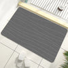A gray, ribbed bathroom mat is placed on a white tile floor next to a wooden tray.