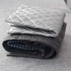 A stack of gray quilted ironing cloths and a folded dark blue plaid shirt on a light gray surface.