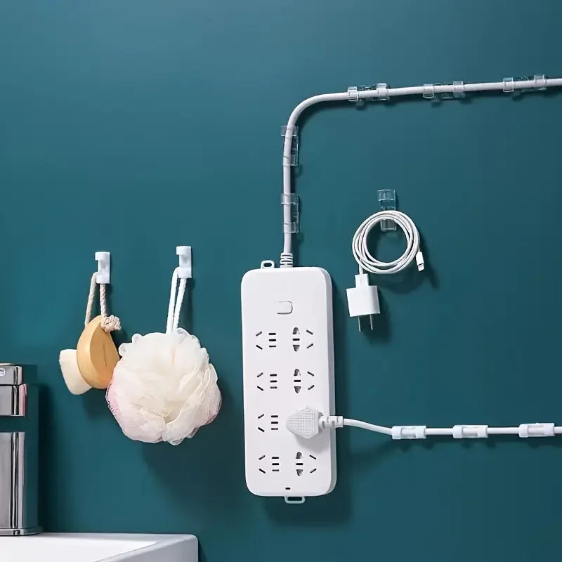 White adhesive cable clips are mounted on a teal wall, organizing electrical cords and cables.